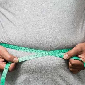 Person measuring waist with green tape measure.