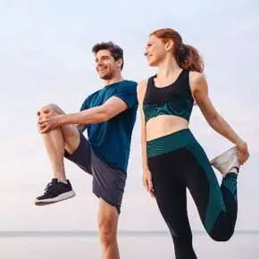 Man and woman stretching outdoors by water.