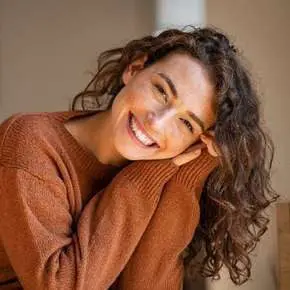Smiling person with curly hair, wearing sweater.